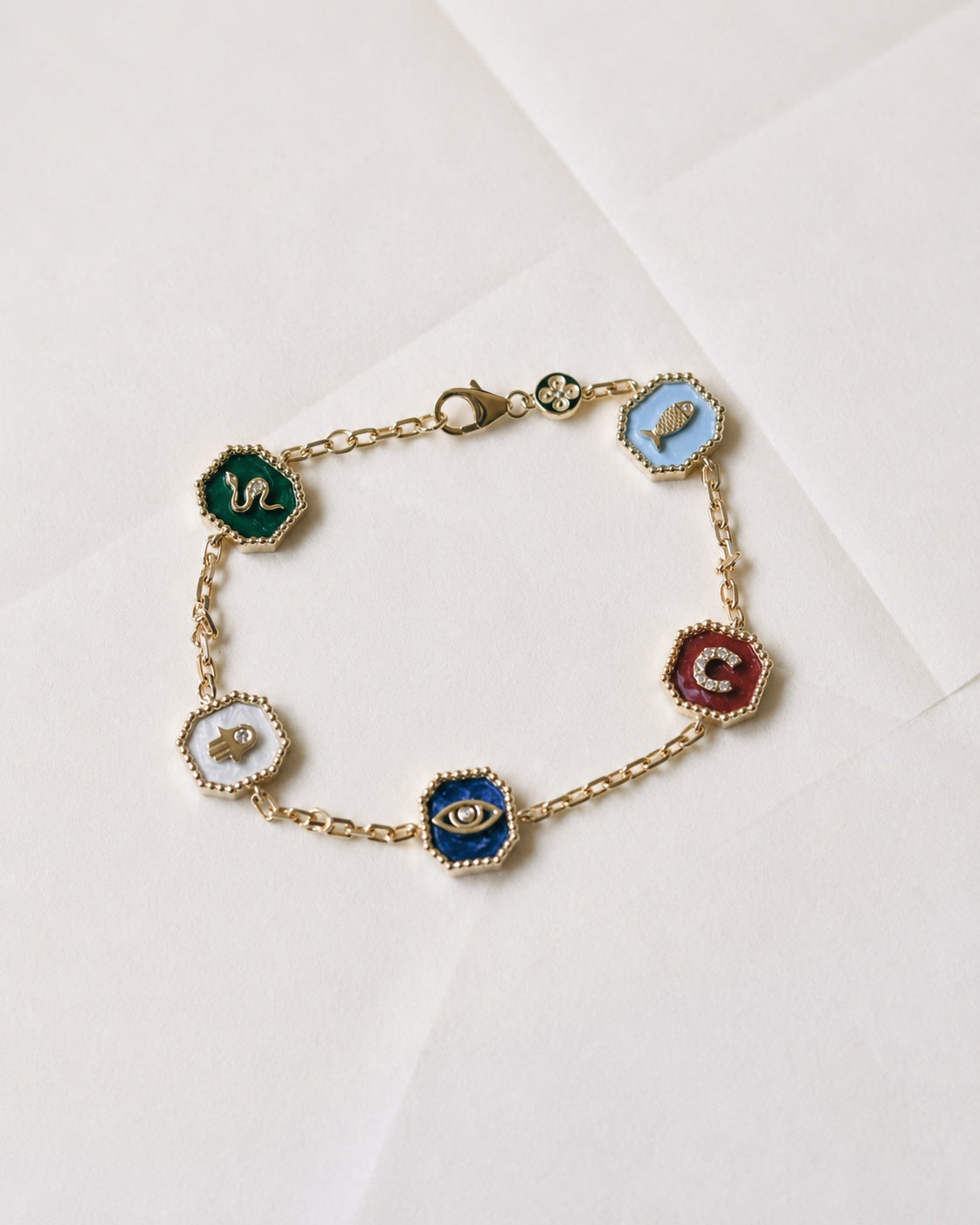 Lucky Medallions gold bracelet with five colourful enamel charms on ivory paper