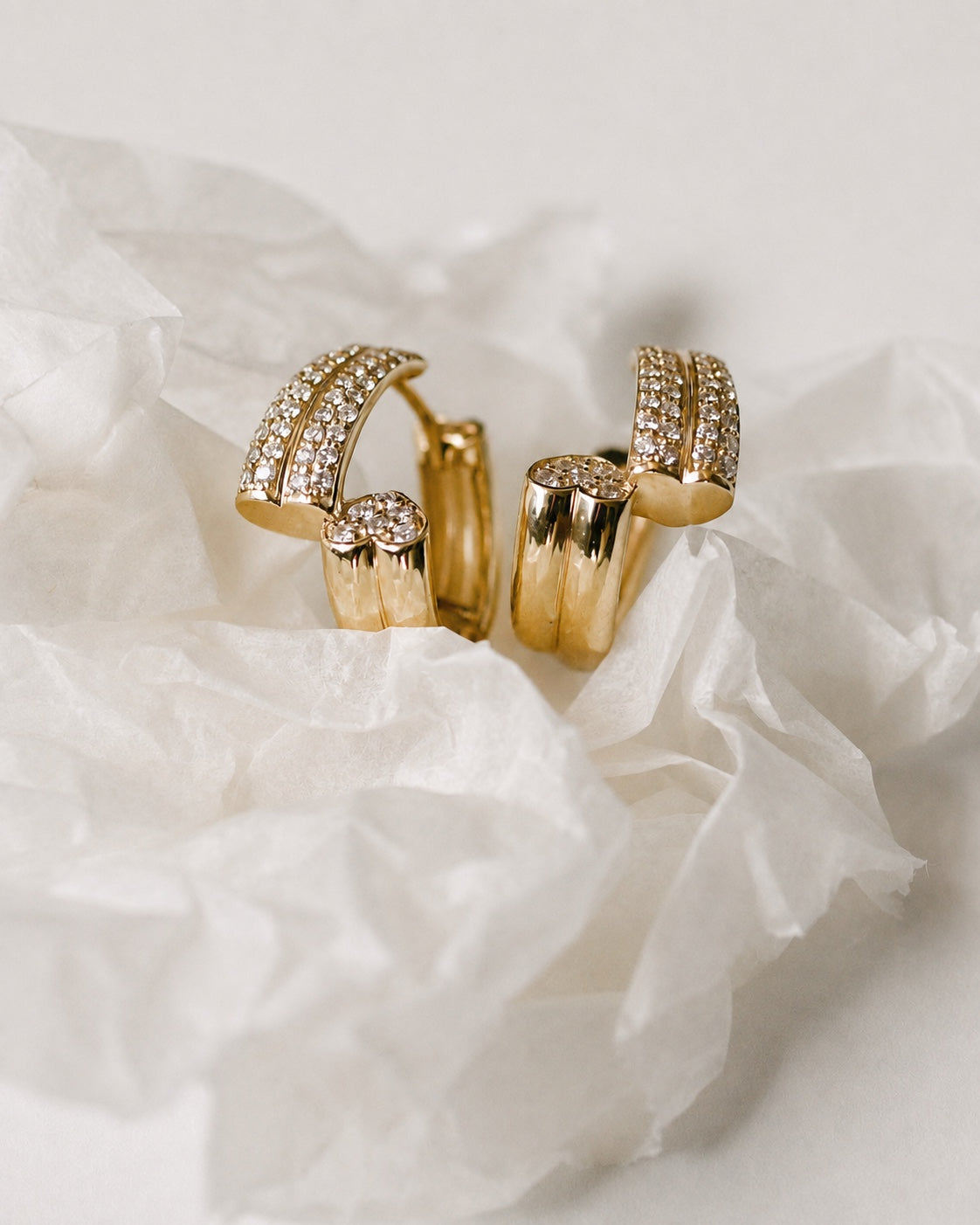 A pair of Heart Duo gold and diamond hoop earrings on ivory tissue