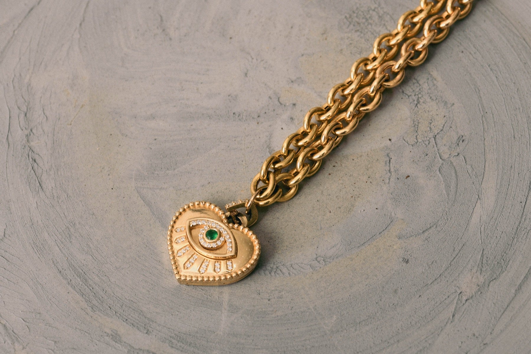 Gold heart and eye pendant with a sculptural chain on grey stone