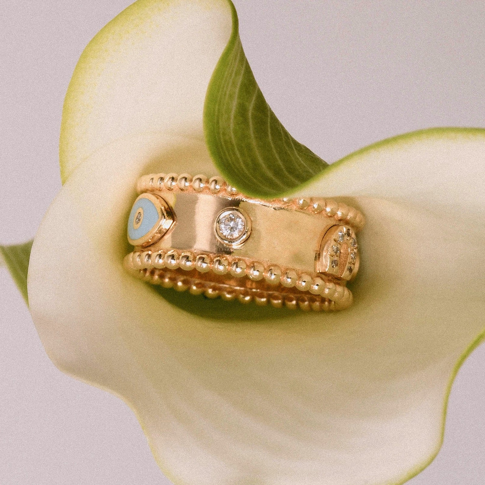 Gold Charms ring with pale blue enamel and diamonds resting horizontally on a calla lily