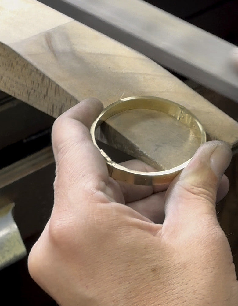 A craftsperson filing a gold bangle at the workbench