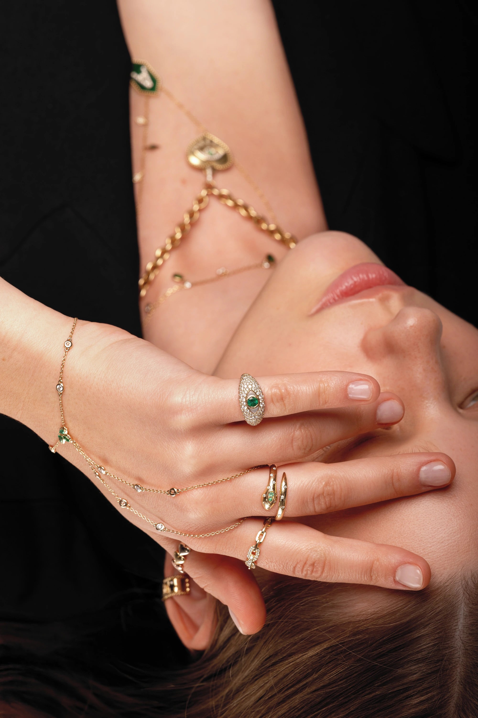 Sculptural gold rings, green stones and hand chains in close detail